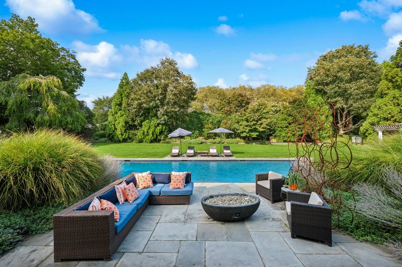 Poolside stone patio with lounge seating and fire bowl at 2 Borden Lane, East Hampton — photo 3 of 12