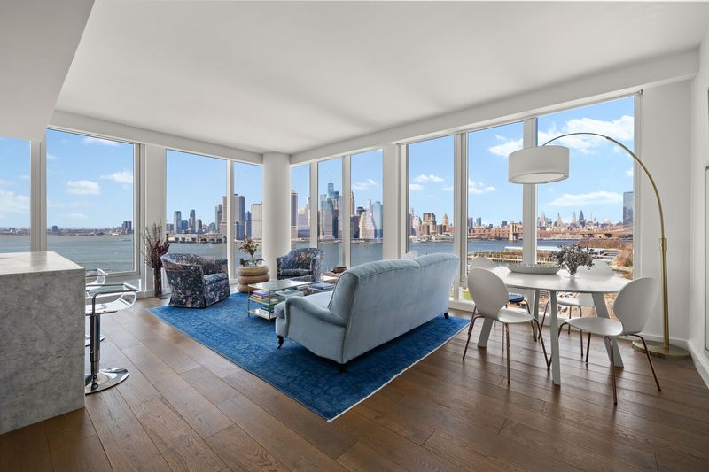 Corner living and dining room wrapped in floor-to-ceiling windows over the harbor at 50 Bridge Park Drive 16B, Brooklyn Heights