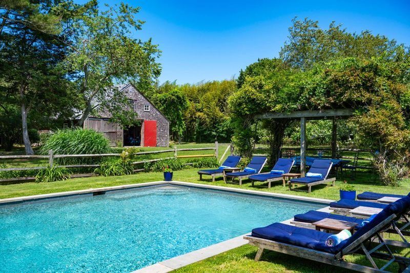 Gunite pool and loungers with the red-door barn beyond at 645 North Sea Mecox Road, Southampton
