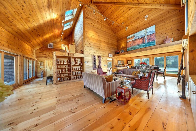 The great room: a soaring cedar cathedral ceiling with skylights, pine floors, built-in bookshelves, a loft-level gallery and glass walls to the garden. at 95 Jobs Lane, Bridgehampton — photo 4 of 12