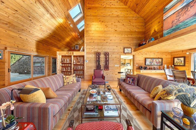 The living area: a long sectional and lounge seating beneath the vaulted cedar ceiling, with clerestory glass and artwork on the gallery wall. at 95 Jobs Lane, Bridgehampton — photo 5 of 12