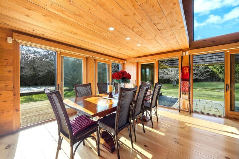 The dining room: a long table between floor-to-ceiling glass doors on both sides, opening to lawn and deck. at 95 Jobs Lane, Bridgehampton — photo 6 of 12