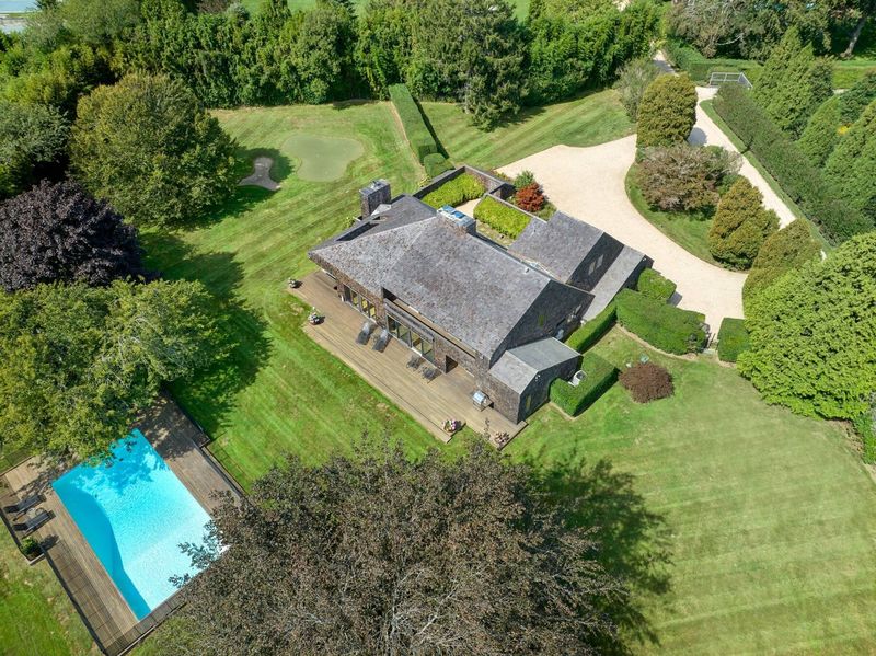 Aerial of the grounds: the house, the heated pool with its surround, hedged lawns and the curving gravel drive. at 95 Jobs Lane, Bridgehampton — photo 8 of 12
